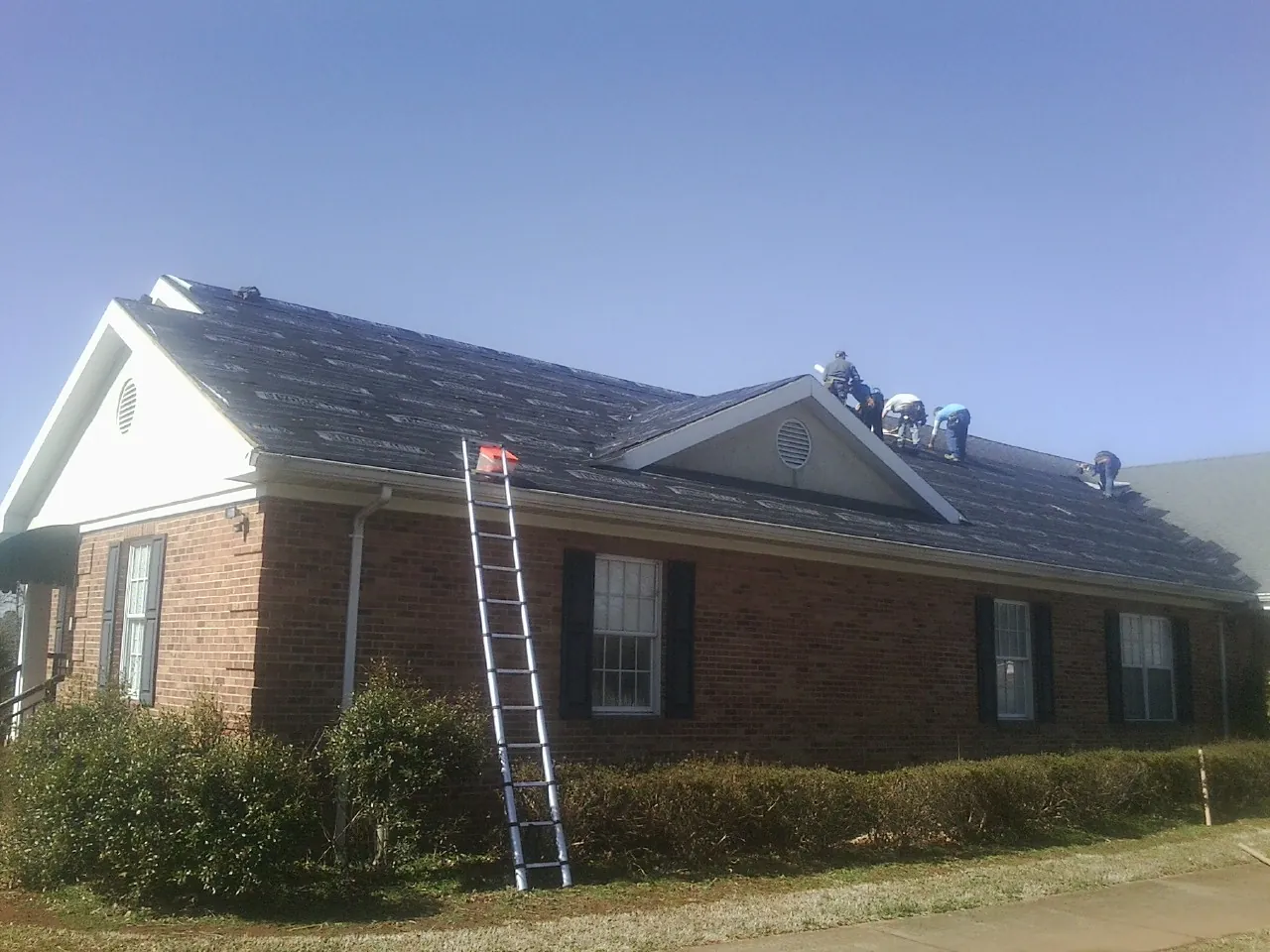 Crew tearing shingles off a brick ranch roof with a ladder set — Metal Roof Repair work by our crew in Round Hill