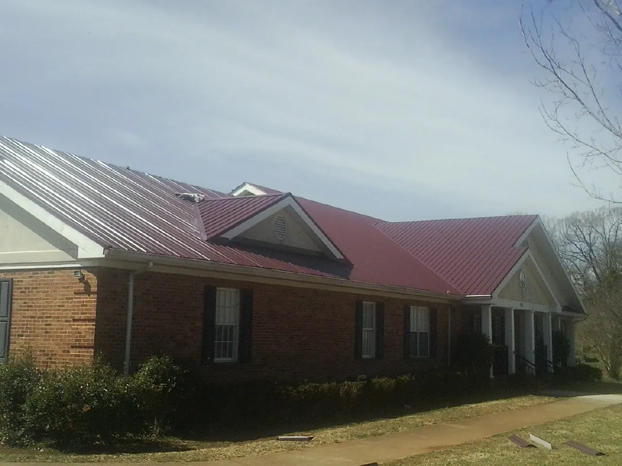 Red metal roof with gabled entries on a long brick building, from a Hail Damage Roof Repair job in Round Hill