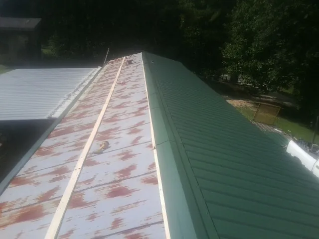 Old rusted panels beside newly installed green metal roofing — Wind Damage Roof Repair by Roofing Brothers in Round Hill