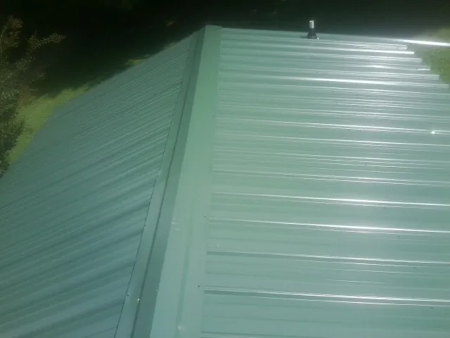 New green metal panels meeting at the ridge of a roof — Flat Roof Repair work by our crew in Round Hill