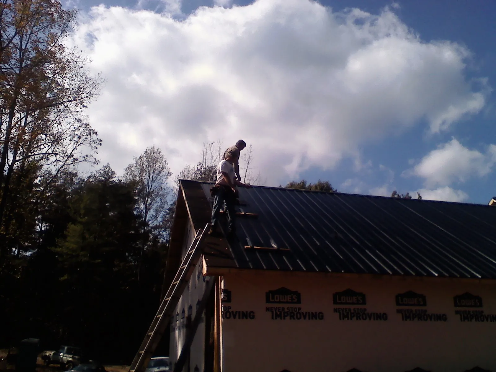 Roofer fastening dark metal panels high against a cloudy sky, from a Roof Inspection job in Round Hill