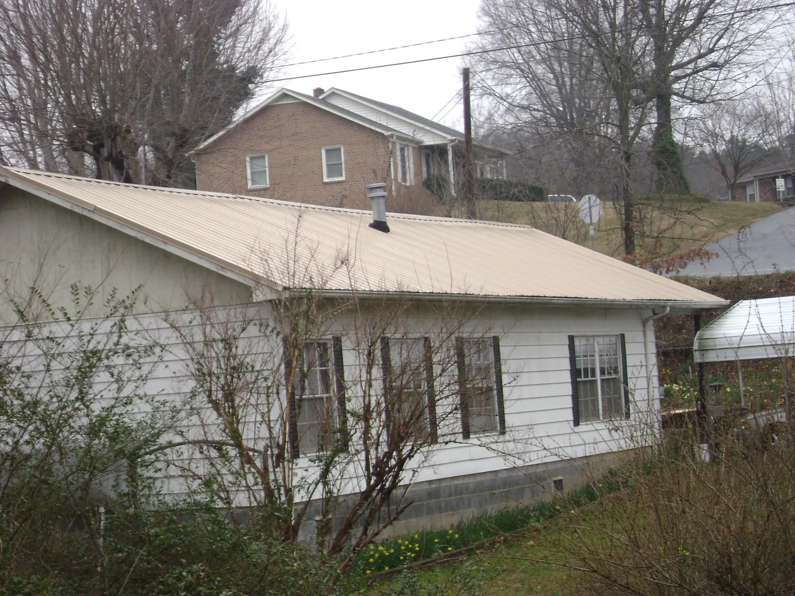 Tan metal roof on a white sided house set into a hillside — Commercial Roofing by Roofing Brothers in Round Hill