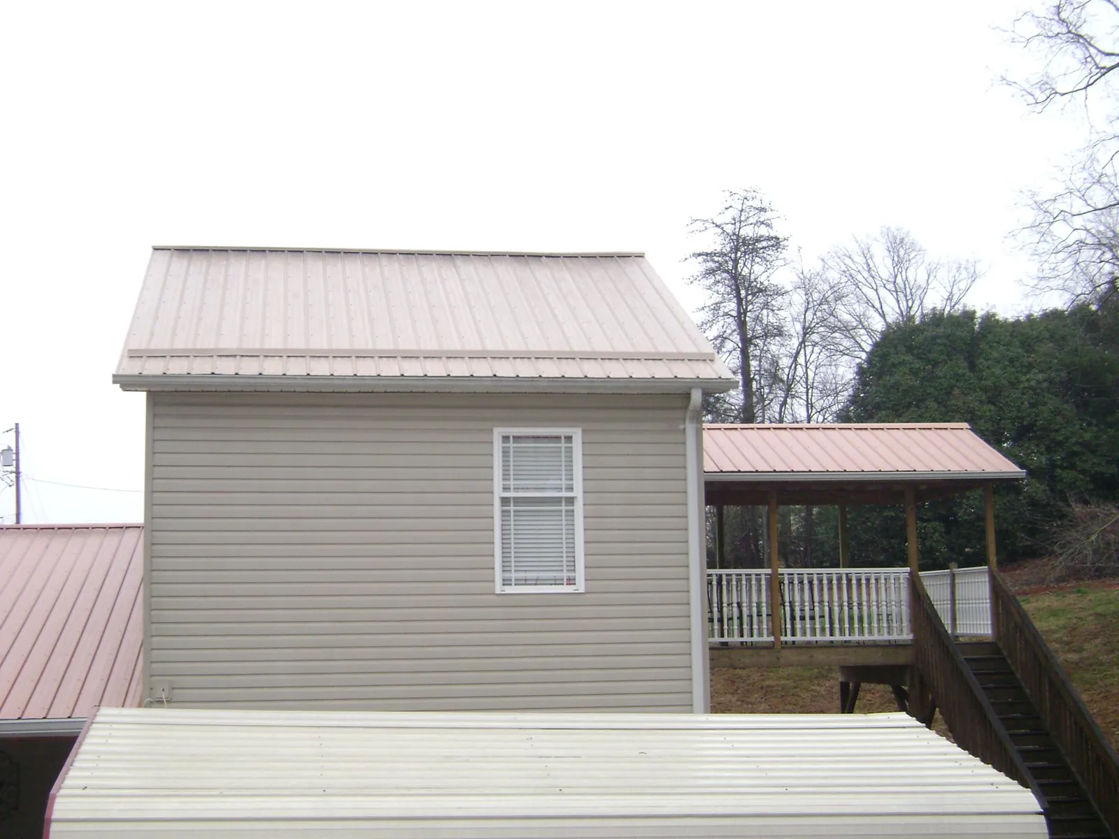 Tan metal roofs on a two story addition and attached porch, from a Roof Replacement job in Round Hill